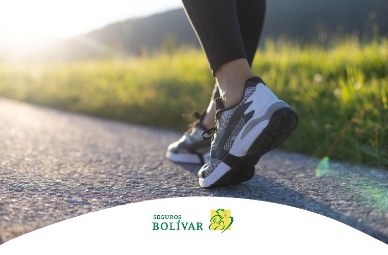 Pies de una persona con zapatillas deportivas caminando por un sendero pavimentado al atardecer en un entorno natural.