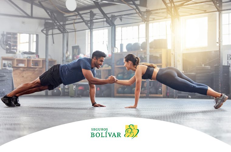 Pareja sonriente haciendo plancha y tomados de la mano en un gimnasio, mostrando cooperación en el fitness.