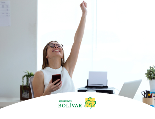 Mujer joven en una oficina, sonriendo con el puño levantado en señal de victoria mientras sostiene un celular, ilustrando éxito o buenas noticias.