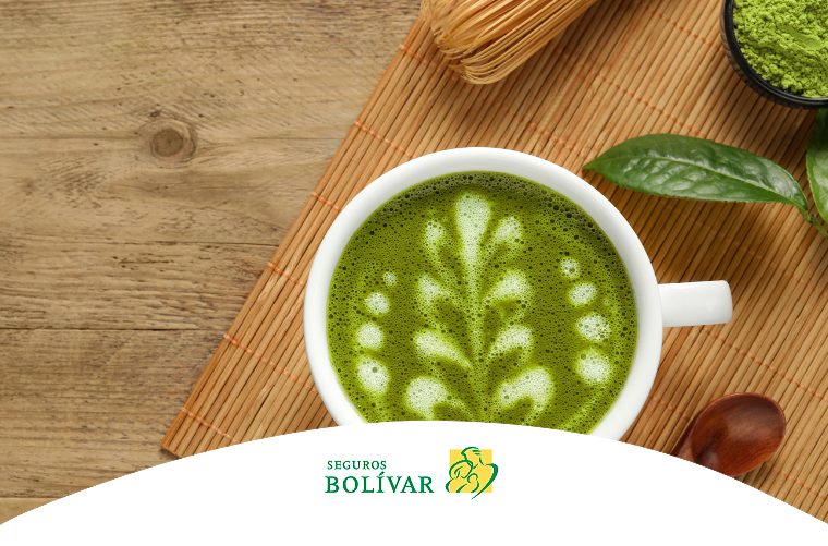 Una toma cenital de una taza blanca de té matcha con arte en la espuma, colocada sobre una esterilla de bambú.