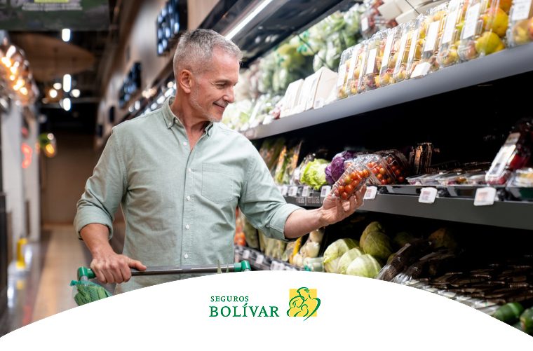 Hombre de cabello canoso sonriendo mientras elige tomates frescos en la sección de frutas y verduras de un supermercado, promoviendo hábitos de compra saludables.