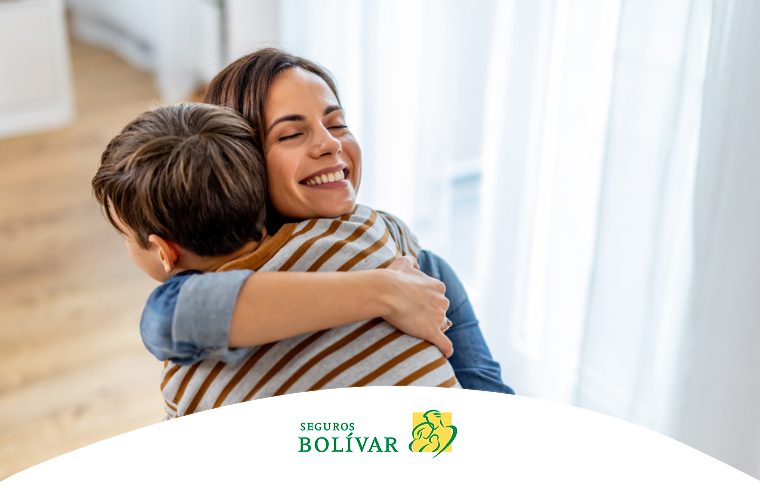 Madre sonriente abrazando cálidamente a su hijo en casa, transmitiendo una sensación de seguridad y bienestar.