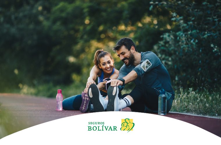 Pareja joven estirando en una pista de atletismo rodeada de árboles, compartiendo un momento de deporte al aire libre.